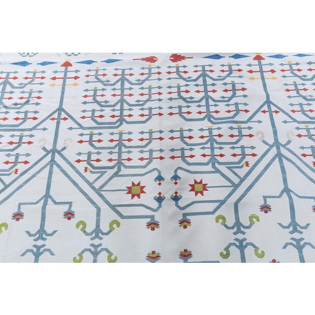This modern Dhurrie rug is a striking celebration of geometry, symmetry, and color, blending traditional flat-weave...
