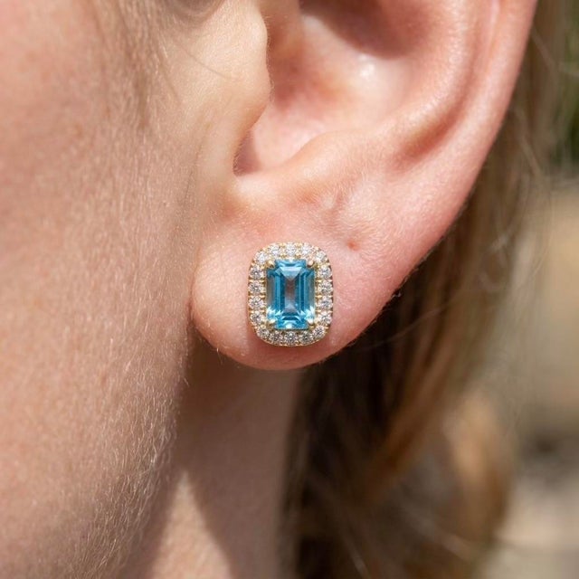 Capture the crystal-clear beauty of cool blue tones with these elegant halo stud earrings, presenting an emerald-cut...