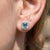 Capture the crystal-clear beauty of cool blue tones with these elegant halo stud earrings, presenting an emerald-cut...