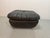 Mid-Century black leather pouf featuring distinctive cord lacing at the corners and decorative brass buttons on the...