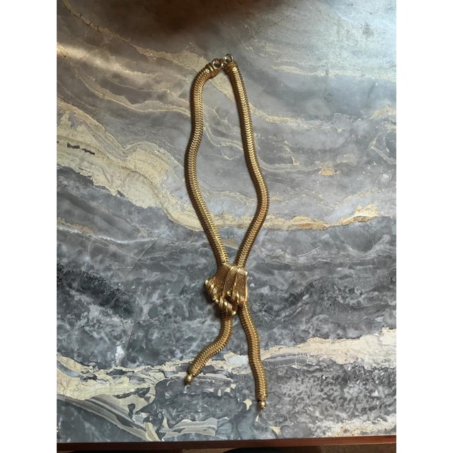This vintage necklace is crafted from a flexible, flat-linked gold-tone chain, often called snake chain for its smooth,...