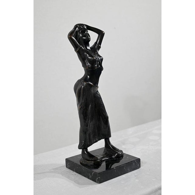 Bronze with brown patina representing a young woman, dressed in a long dress, with a swaying look. This protagonist,...