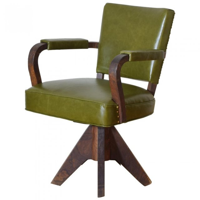 Elegant French Art Deco–style swivel chair featuring olive green leather upholstery, gracefully curved hardwood arms, and...