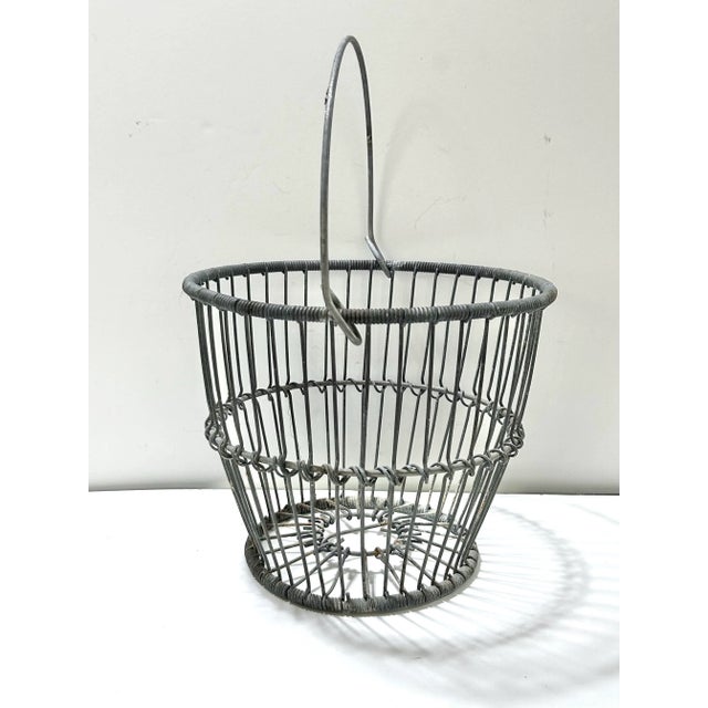 An authentic 1920s zinc wire egg gathering basket featuring a sturdy arched handle and classic open wire construction. The...