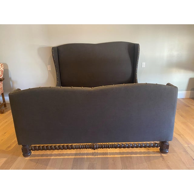 This is a dark gray upholstered wingback bed with footboard. The most distinctive feature is the bobbin-turned or spool-...