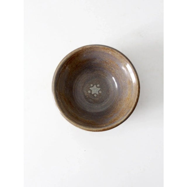 This vintage handmade studio pottery bowl shows soft tonal variation in an earthy brown glaze, with a star motif at the...