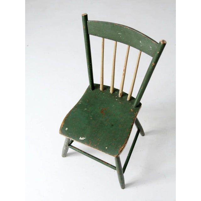 Antique primitive chair with a rustic plank seat, spindle back, and graceful splay legs. The aged green painted finish,...