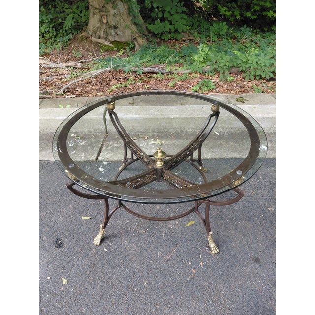 A handsome vintage neoclassical-inspired coffee table featuring a sculptural iron frame with brass accents and a beveled...