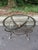 A handsome vintage neoclassical-inspired coffee table featuring a sculptural iron frame with brass accents and a beveled...