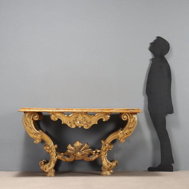 Baroque console table in carved and gilded wood. Wooden top with painted faux marble finish, four S-shaped legs richly...