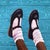 The artwork presents a close-up view of a child's feet adorned in shiny black shoes, accented by white ankle socks, set...