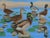 Brightly colored and crisply detailed painting of a group of mallard ducks resting on stones on a calm lake, their dappled...