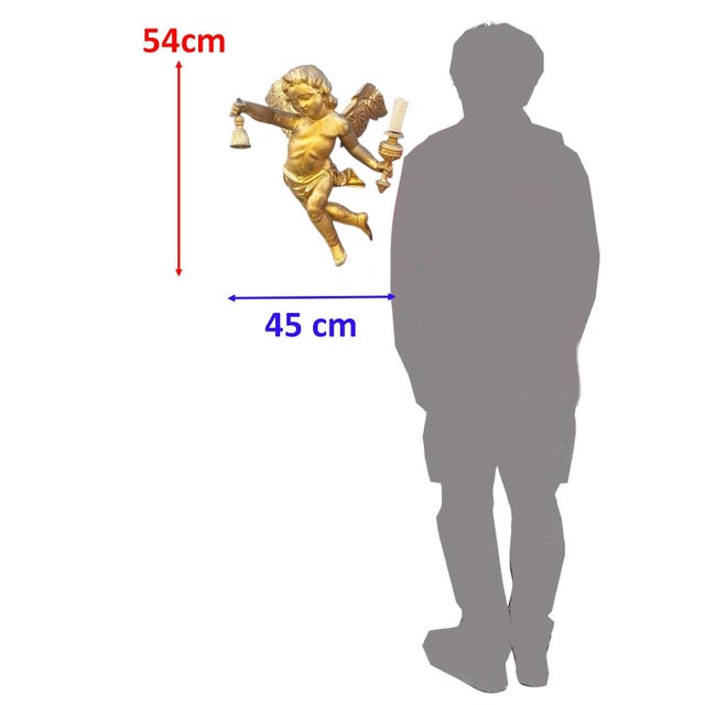 Winged putto in gilded wood, holding a candlestick in his left hand. Some chips and wear to the gilding and old...