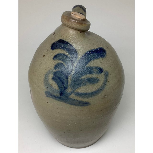 Antique salt-glazed stoneware jug is a Cowden & Wilcox piece from Harrisburg, Pennsylvania, featuring distinctive cobalt...