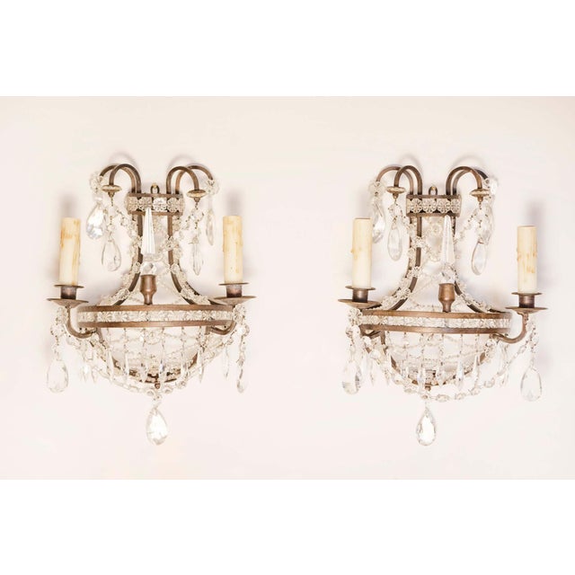 A pair of French Directoire style two-light wall sconces from the 20th century with bronze armature, crystal rosettes and...