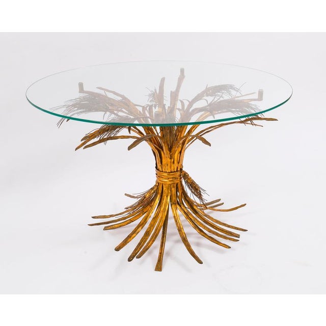 A striking Hollywood Regency coffee table with a gilded tole metal “Sheaf of Wheat” sculptural base and a glass top,...