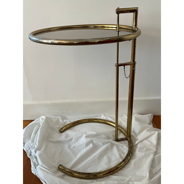After Eileen Gray's E 1027 adjustable round chrome and glass side table This one in a brass finish with tinted glass....