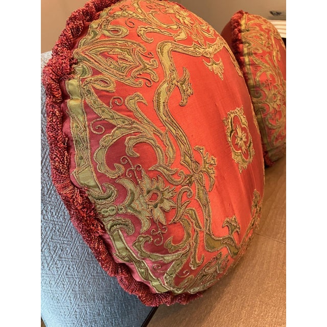 A pair of matching round, silk pillows in a beautiful rose/crimson red. The pillows are trimmed with a brush fringe in a...