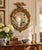A Federal-style giltwood convex mirror crowned with a carved eagle, its wings outstretched above a laurel motif—an...