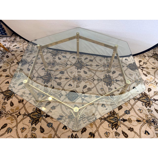 A sculptural Hollywood Regency statement piece featuring a thick beveled glass top set over an ornate polished brass base....