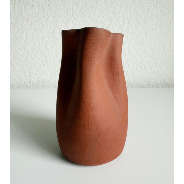 Early 21st-century organic modern redware vase featuring a pinched or rippled neck. Matte terra cotta colored exterior...