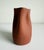 Early 21st-century organic modern redware vase featuring a pinched or rippled neck. Matte terra cotta colored exterior...