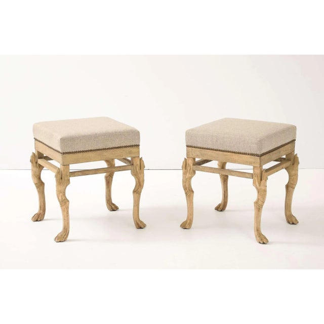 Pair of square hoofed-foot stools in bleached wood, newly upholstered in neutral linen with brass nail-head trim—perfect...