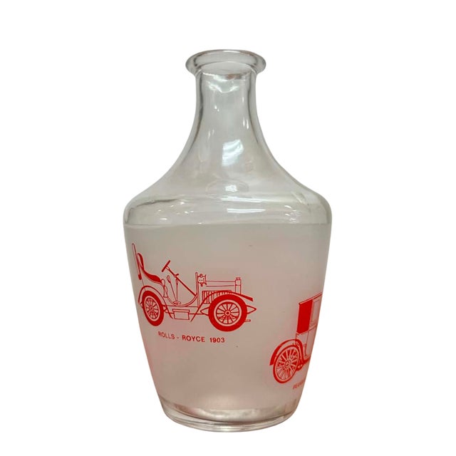 A charming vintage French glass decanter featuring vibrant red illustrations of some of the earliest automobiles,...