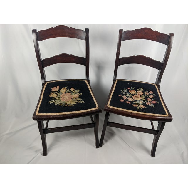 A charming pair of vintage dark wood side chairs featuring beautifully detailed floral needlepoint seats, gracefully...