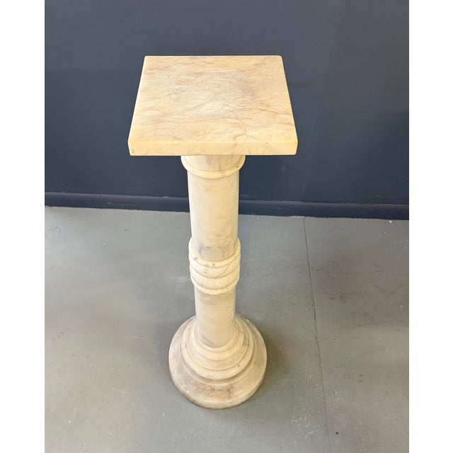 This elegant carved alabaster column features a classical architectural form rendered in softly veined, warm-toned stone....