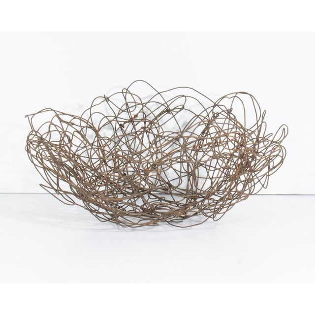 A handwoven metal basket. This metal basket is composed of wires that are woven to create a bowl-shape form. The basket is...