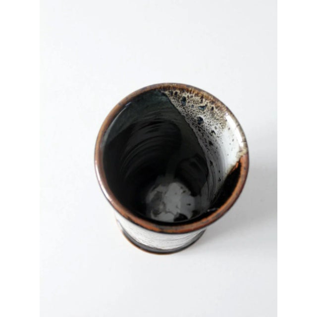 This is a vintage studio pottery vase. Signed by the artist, the tall hand-crafted vase features a sweeping black, white,...