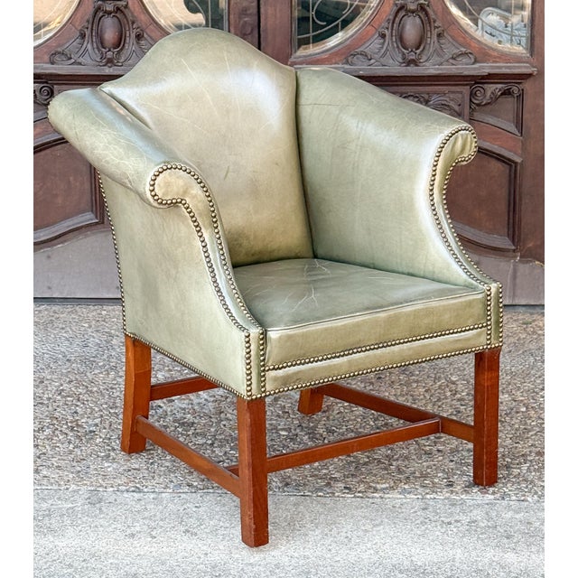 A fine English wingback library lounge armchair - upholstered in patinated green leather on a wooden frame - in the George...