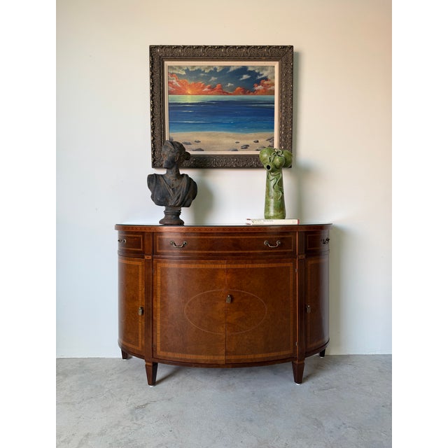Elegant and timeless, this vintage Regency-style demilune sideboard features a beautifully curved half-round silhouette...