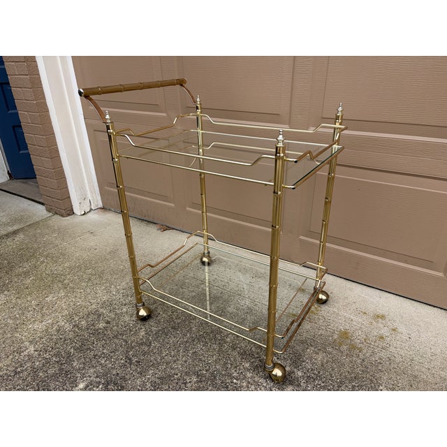A gorgeous Mid-Century Hollywood Regency faux bamboo brass and glass rolling bar cart USA, Circa 1960s Measures: 27"W x...
