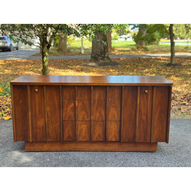 Mid-century modern credenza featuring richly figured wood grain, architectural vertical detailing, and a warm walnut-toned...