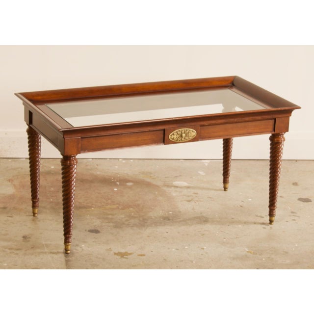 A handsome Regency-style cocktail table with British Colonial flair. A raised tray-top gallery frames an inset glass top,...