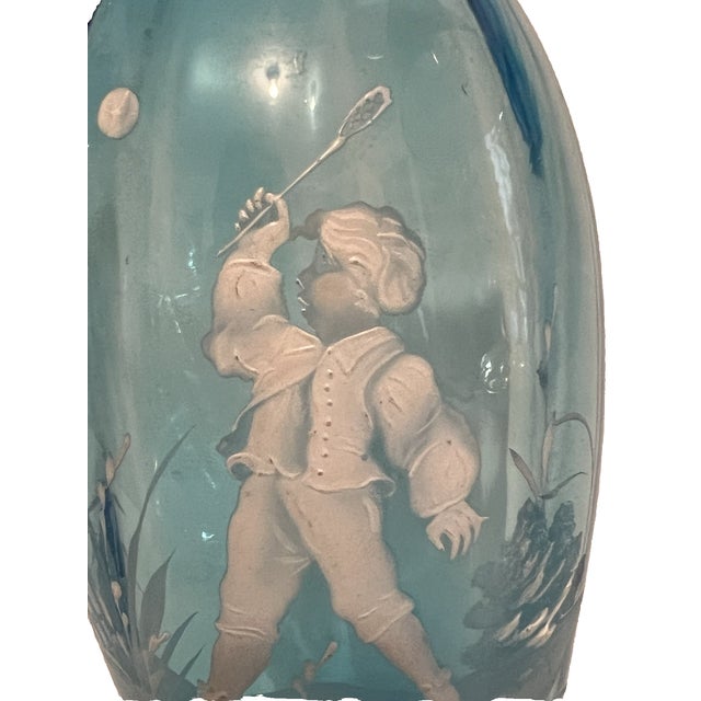 The Mary Gregroy Blue Glass Vase is an antique piece hand-painted with white enamel, featuring a child boy playing in a...