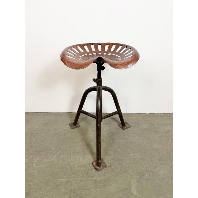 Vintage industrial three-legged height adjustable swivel chair from the 1950s. An old tractor seat mounted on an iron...