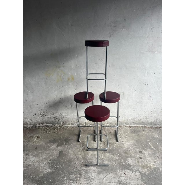 Introduction A set of four industrial bar stools featuring tubular metal frames and round burgundy seats. Their minimal,...