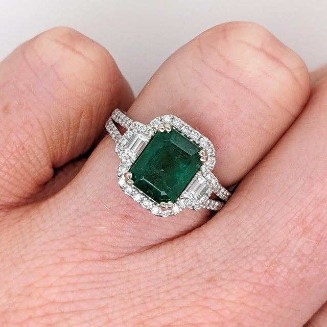 This statement ring has a vintage style emerald surrounded by a natural halo of diamonds and baguette diamond accents....