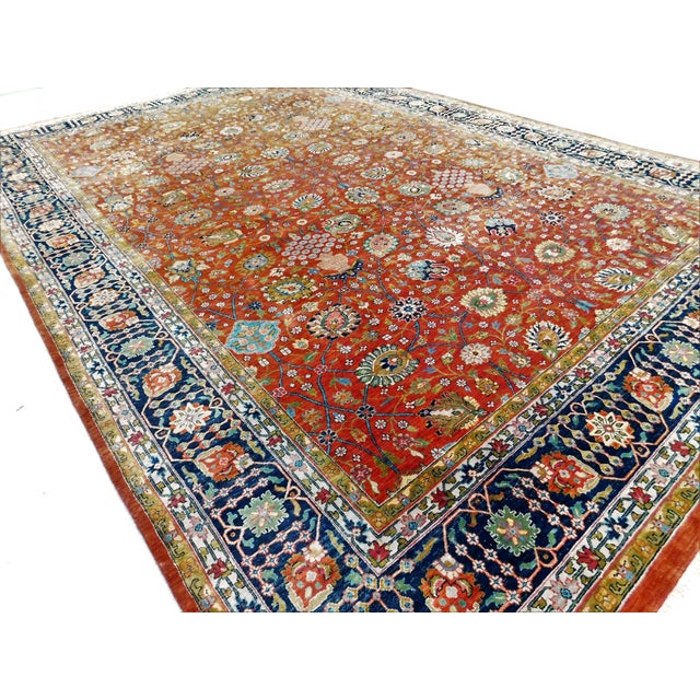 Vintage hand-knotted Persian rug with vibrant rust field adorned with detailed floral and vine motifs, framed by a...