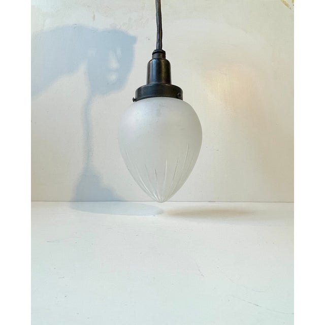 A 1930s ceiling light composed of a black bakelite top and set with a drop shaped shade in opaque partially cut crystal...