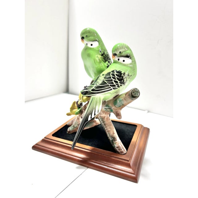 Charming mid century porcelain parakeet sculpture featuring two vividly detailed birds perched on a naturalistic branch. A...