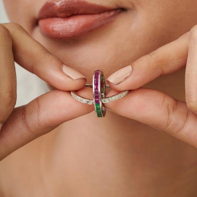 A refined 925 sterling silver spinner eternity band featuring a vibrant combination of natural emeralds, rubies, and...