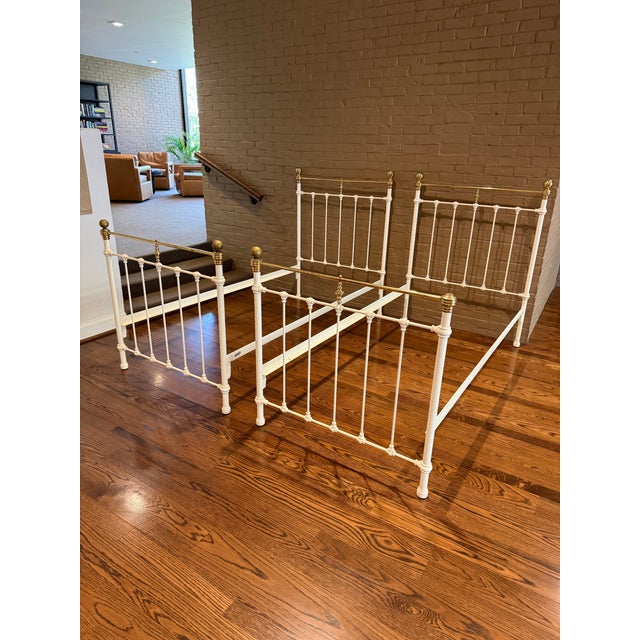 Pair of traditional brass and iron antique twin beds. Beds are painted white with decorative castings on the head and foot...