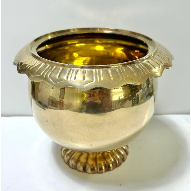 A striking Hollywood Regency brass cachepot featuring a fluted pedestal base and sculptural rim detail. Its polished brass...