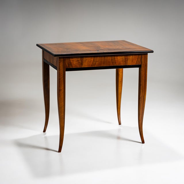 Elegant Biedermeier table featuring four gracefully curved legs and a small drawer. The surface is walnut-veneered, with...
