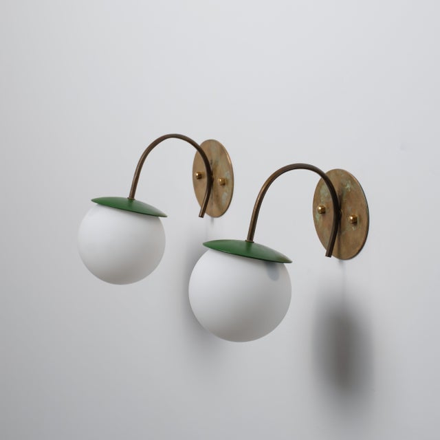Pair of italian wall sconces dating from the 1950s, featuring curved brass arms, round brass wall plates and spherical...
