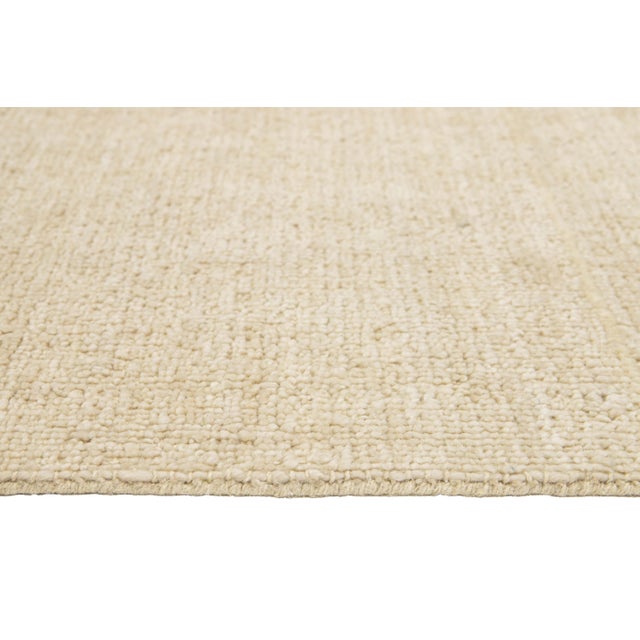 This modern Indian handknotted wool rug is skillfully woven by artisans and features a solid design. Its soft beige hue...